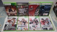 Eight Xbox 360 games in cases arranged in two rows on a surface, showing covers of Fable III, Grand Theft Auto IV, Forza Motorsport 3, Halo 3 ODST, NCAA 07 March Madness, Madden 11, NHL 11, Tiger Woods PGA Tour 11.