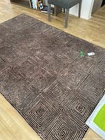 Rectangular area rug laid on hardwood floor showing black and brown diamond/square geometric pattern.