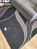 Area rug spread flat under sofa showing abstract wave design and some signs of wear and dirt.