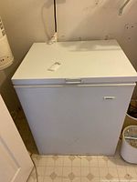 Closed white Galaxy chest freezer on a tiled floor near a white wall and heating unit.