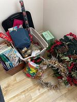Overview photo showing multiple bins and containers of Christmas ornaments, a colorful tie-dyed gift bag, and several rolled wrapping papers. Also shows a green cardboard gift box.