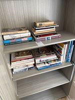 Top and front view of a shelf with 18 assorted cookbooks by various authors in different sizes and conditions.