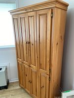 Front and side view of the wooden corner hutch closed, showing natural wood finish, paneled doors, and wooden knobs.