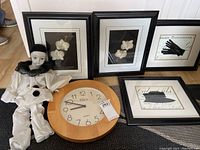 Lot overview showing four framed art pieces, porcelain-faced doll, and round wooden frame clock