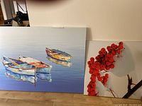 Two framed canvas prints leaning on floor: one large 24x36 inch canvas with boats and a smaller 20x20 inch canvas with winter berries