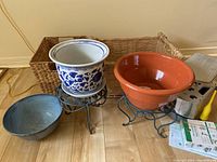 Photo of the flowerpots on black metal stands, gray ceramic bowl, and wicker basket in background