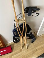 View showing the wooden crutches leaning on the folded rollator concentrating on handles and wheels.