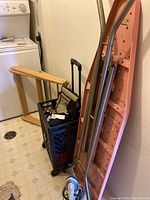 A general photo of the lot showing the stacked items including the drying rack, ironing board, shopping cart, and iron on the floor in a laundry room setting.