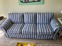 Front view of the 3-seater sofa with blue and white striped slipcover, showing three seat cushions and three back cushions, rounded arms and skirted base, in a well-lit room.