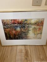 Framed original dye on silk painting showing river landscape reflecting autumn trees, with beige mat and gold frame.