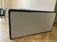 Top view of one black fabric single bed box spring lying flat on wooden floor.