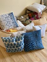 Image showing assortment of various throw cushions in different patterns and colors stacked on floor and surface.