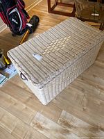 Full view of wicker trunk closed, showing woven diamond pattern on lid and dark handles.