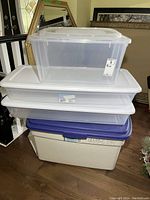Four plastic lidded storage bins stacked; two large clear Sterilite bins on top, smaller clear bin above a large beige Rough Tote bin with navy lid