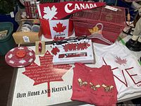 Photo showing assortment of Canada Day themed items including flags, metal bucket, wire baskets, T-shirts, wall art, and other decor items.
