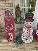 Full view of two items: snowman decoration with string lights and wooden Merry Christmas sign leaning against wall.