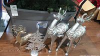 Bin of green garland, smaller gold tone reindeer figurine, small decorative golden Christmas tree, and two large silver resin reindeer.