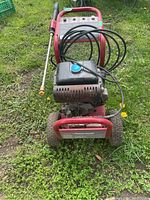 Full view of Coleman Powermate pressure washer showing hose and spray wand attached, situated on grass.
