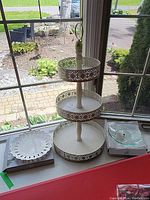 View of the stand alongside the porcelain dish with scalloped edges and clear glass candy dish without a stand, all displayed together on a windowsill.