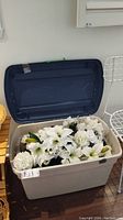 Full view of large plastic bin with lid open, showing a variety of white faux flowers inside.