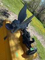 Photo showing large resin fairy figurine with wings and detailed face next to resin statuette of two children on an outdoor yellow surface.
