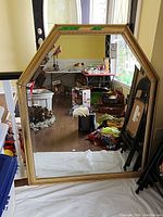 Full view of large octagonal framed mirror leaning against a wall indoors reflecting various household items.
