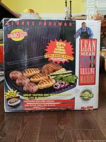 Front view of original boxed George Foreman Lean Mean Fat Grilling Machine jumbo size grill with promotional graphics showing grill, foods, and George Foreman.
