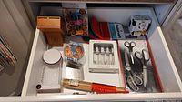 Overview of all kitchen items arranged in drawer showing oven mitts, utensils, clips, bowl and packaging for cheese pod.