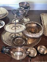 Overview of lot showing various silver plated items including gravy boat, two tiered tray, large bowl, coffee pot, and handles of cream and sugar cups