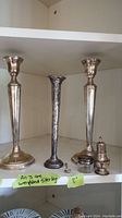 Two tall sterling silver weighted candle holders flanking a textured silver vase, along with a glass jar with silver lid and a small salt shaker on shelf