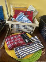 Photo of plastic storage bin filled with folded tea towels and oven gloves, a few tea towels and oven gloves laid out in front on round placemats in yellow and green.