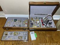 Wood jewellery box open showing removable tray and drawer with multiple pieces of costume jewellery arranged inside.