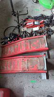 Photo showing two red metal vehicle ramps alongside jack stands, tire irons, a chain, and hydraulic jacks on concrete floor.
