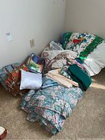Full lot showing multiple bedding items including folded and stacked bedspreads, pillowcases, and colorful Disney themed quilt.