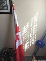 Full view of the Canadian flag on the wooden pole leaning against a wall, showing the flag's design and size.