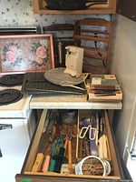 Kitchen counter and drawer containing multiple kitchen items including cast iron pans, warming tray, electric can opener, spice racks, and utensils.