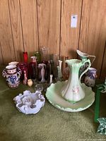 Overview of ceramic pitcher and wash basin surrounded by multiple colored glass vases, ceramic pottery jar, and candle holders.