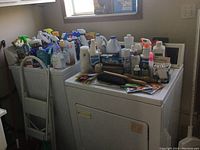Wide view of lot showing step stool behind washing machines with various cleaning bottles on top.