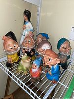 Photo showing Snow White standing behind the seven dwarf figurines with the frog and elf in front on a wire rack shelf.