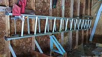 Side view of the full ladder hanging on shed wall showing aluminum rungs and frame, separated into two pieces.