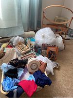 Assorted crafting materials including yarn, batting bags, zippers, magazines, fabric scraps, and knitting needles on carpet near window.