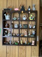 Full front view of dark-stained wood shelf filled with a collection of ceramic and porcelain figurines and mini dishes.