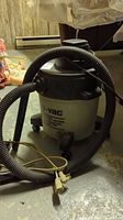 Full view of a gray and black Shop Vac wet/dry vacuum with coiled black hose and attached power cord on the floor.