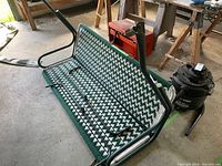 Porch swing with green and white woven patterned seat and green painted metal frame along with stand framing in a workshop environment.