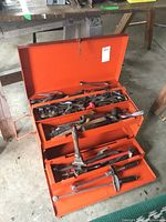 Orange metal toolbox open showing two-tiered trays filled with assorted hand tools including wrenches, hammers, and pliers.