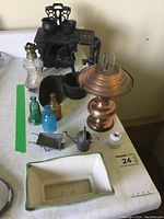 Full lot overview showing all included miniature items arranged on table including cast iron stove, pots, oil lamp, funnel, mini wheelbarrow, watering can, glass bottles and ceramic tray.