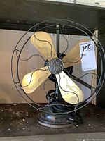 Front view of vintage General Electric table fan with brass blades and protective wire cage on shelf.