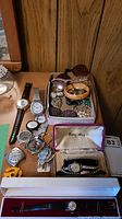 Lot overview with assorted wristwatches, brooches, bracelet, and eyeglasses on wooden surface