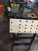 Ultra Steel workmate bench with wooden perforated top and attached hand saw, viewed from above.