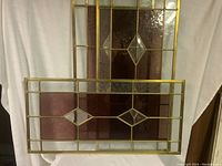 Photo showing three glass window panes with brass-colored metal framing and diamond-shaped geometric patterns.